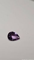 Photo showing pear cut natural purple amethyst gemstone with good clarity and deep purple color under neutral lighting.