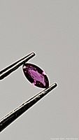 Close-up photo of a marquis cut natural ruby gemstone held by tweezers, showing deep fuchsia color and clarity.
