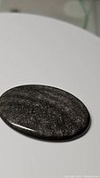 Polished oval natural silver sheen obsidian cabochon showing the silver reflective surface on black base.