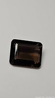 Close-up photo of a dark brown emerald cut smokey quartz gemstone on a plain background.