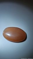 Oval peach moonstone cabochon with smooth polished surface laying flat on white background showing natural shimmer.
