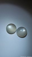 Photo of two round white moonstone cabochons showing their smooth, polished surfaces and characteristic moonstone flash.