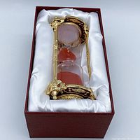 Gold-plated Baroque-style hourglass sand timer in its red and white gift box with satin lining.