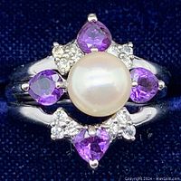 Close-up of a sterling silver ring with a large white pearl center and four purple heart-shaped amethysts with clear accent stones surrounding the pearl.