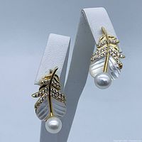 Pair of gold plated earrings featuring 5mm pearls and leaf design with shell and crystals on white stand