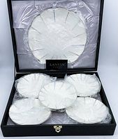 Six Lanvin plates with scalloped edges and colored line accents nestled in black box with satin lining, showing original packaging and presentation