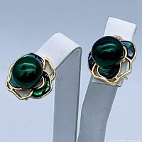 Front angled photo showing pair of black pearl earrings on white stand, highlighting shell petal design and gold plating.