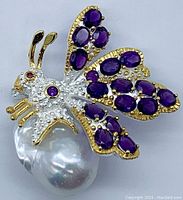 Front view of bee brooch on white background showing amethyst pavé wings, rhodolite accents, baroque pearl and gold plating