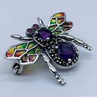 Close-up front angle of brooch showing amethyst stones, enamel wings, ruby eyes, marcasite accents and silver legs