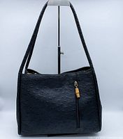 Front view showing black ostrich leather texture and vertical zip pocket with wooden zipper pull.