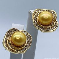 Pair of golden South Sea pearl earrings displayed on white stand