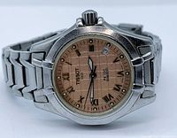 Front view of Tissot PR100 ladies watch showing peach dial with Roman numerals and date window.