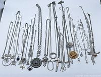 Overview of the entire assortment of silver-tone necklaces with assorted pendant designs displayed on white background.