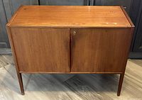 Front view of teak bar cabinet showing two doors, sculpted handles, and lock plate