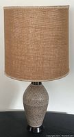 Front view of the table lamp showing beige ceramic base and tan burlap lamp shade against a white wall.