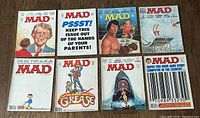 Eight vintage Mad Magazine issues arranged on a wooden floor. Varied illustrated covers depicting caricatures and satirical scenes. Includes issues #190, 194, 195, 197, 198, 204, 205, and 210.