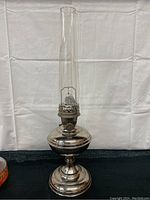 Full front view of the antique Aladdin oil lamp showing metal base, burner assembly, and tall clear glass chimney.