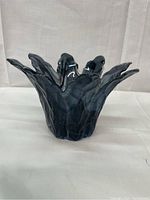 Front and side view of dark art glass candle holder with petal-shaped edges on white fabric background.