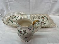 Set of three floral porcelain pieces: one pitcher and two decorative bowls with gold accents