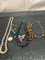 Photo showing six different costume jewelry necklaces laid out on a dark surface.
