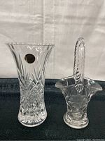 Photo of two clear crystal vases, one tall with label, one smaller basket-shaped with handle.