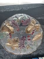 Top angled view of the glass bowl showing colored raised grape clusters and leaves design in purple, red, green, and gold tints.