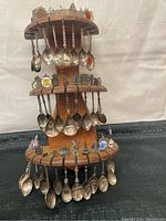 Full view of a wooden stand displaying about 32 silver plated mini souvenir spoons arranged on three tiers.