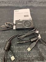 Nikon Coolpix S3700 camera front view with USB cable and manual