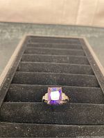 View of sterling silver ring with square purple gemstone on black display tray