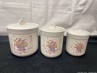 Three ceramic canisters of varying sizes arranged side by side showing front floral basket design