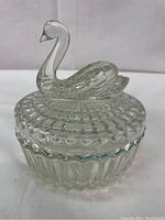 Front view of vintage clear glass powder container with molded swan lid showing detailed swan figure and faceted base sides.