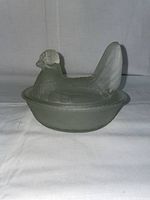 Frosted glass hen on nest dish, shown in front view, sitting on a fabric surface with white background.