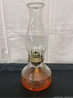 Full view of the vintage hurricane lamp showing the orange glass base with texture pattern, clear tall chimney, and metal burner with wick inside.