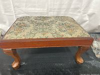 View of the wooden stool from a side angle showing the ornate curved legs and floral upholstered top.