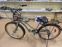 Left side view of the green vintage women's bicycle focusing on the frame, front basket, and tires, showing condition and features
