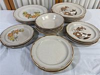 Set of Baroque stoneware large plates with floral patterns in orange and brown, small plates with speckled beige glaze and brown rim, and bowls with similar finish, arranged on table