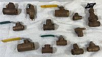Lot of mixed brass plumbing connections and valves including ball valves with lever handles and threaded fittings laid out on white towel