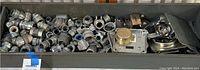 Wide shot of a tray filled with a large collection of galvanized steel electrical conduit connectors and fittings including elbows, caps, and couplings.