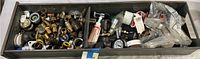 A wide view of a metal tray containing assorted plumbing and electrical components including brass fittings, valves, connectors, and plastic parts.