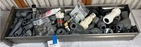 Wide shot showing a rectangular metal tray filled with various gray and white plastic plumbing and electrical parts including fittings, couplings, connectors, and adapters.