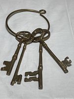 Photo showing four vintage brass keys attached to a large brass ring, displaying the length and design of the keys.