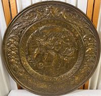 Front view of the circular brass wall plaque with detailed repousse depicting a pub scene and ornate floral border