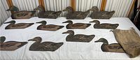 Twelve vintage fiber board mallard duck decoys arranged on a white surface, all double-sided and showing painted mallard details.