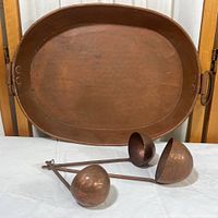 View of large hammered copper tray with three nested copper ladles in front.