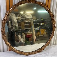 Front view of round mirror showing reflective surface and ornate composite frame with floral and leaf patterns.