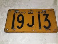 Front side of 1942 Ontario license plate showing alphanumeric code 19 J 13, crown emblem, and dated 1942 in black on yellow background.