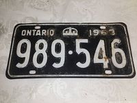 Front view of the 1963 Ontario license plate showing embossed white numbers 989·546, with white text 'ONTARIO' and '1963' separated by a crown symbol, on a black metal plate.