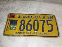 Front view of the 1970 Alaska license plate showing the embossed blue numbers, state flag, date stickers from 1974 and 1972, and the slogan 'North to the Future'.