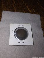 Front view of the 1918 Canadian penny inside a white protective cardboard sleeve secured with staples, coin visible through the plastic window.