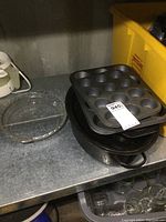 Photo showing black enamel roasting pans stacked, metal mini and regular muffin pans stacked on top
